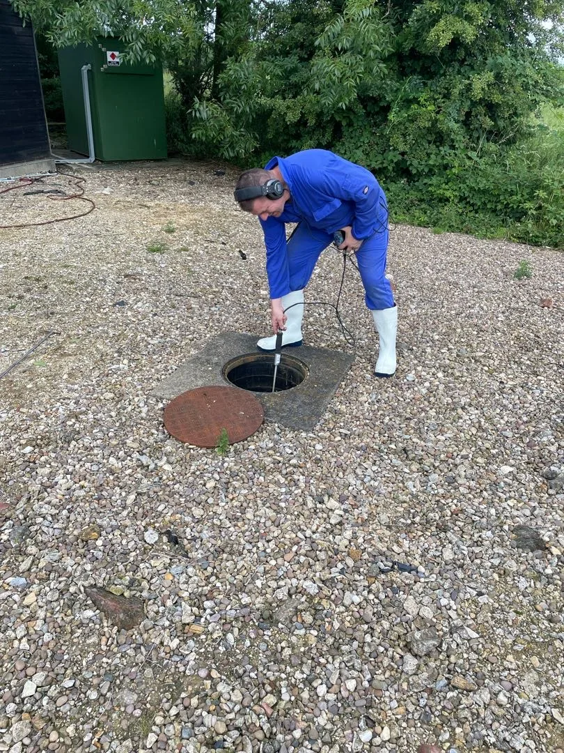 Engineer inspecting an open drainage chamber with listening equipment